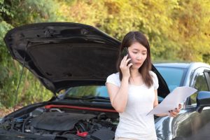 Person on the phone calling their insurance adjuster with car behind them and hood raised.