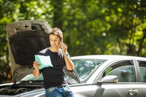 A person looking at their insurance claim while sitting on their car calling their insurance company