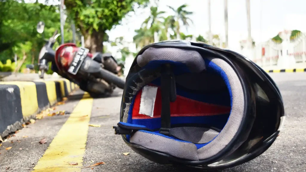 A motorcycle helmet lying on the ground near a fallen motorcycle, with palm trees in the background