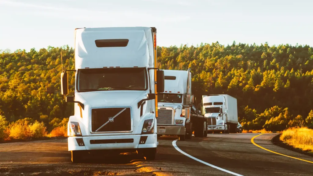 A row of white trucks driving along a winding highway with green hills in the background