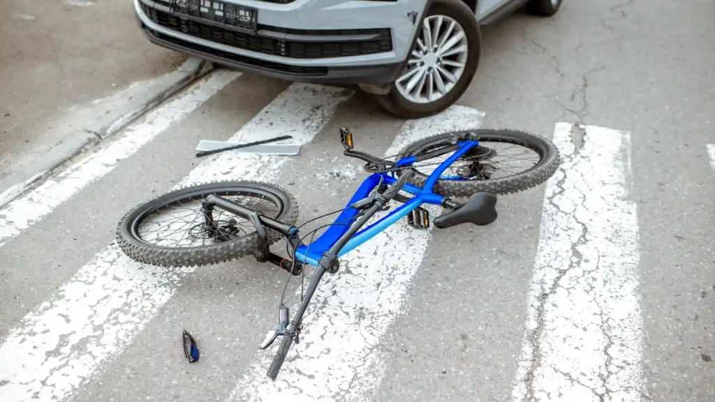 A blue bicycle is on the road, partially crushed by a car, showing signs of a recent accident.