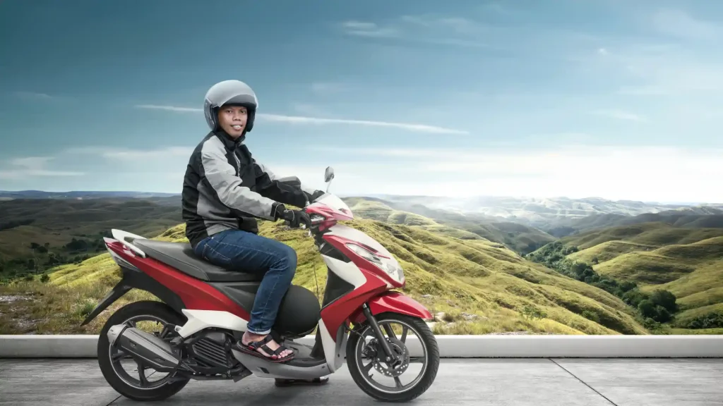 Person wearing a helmet riding a red scooter on a scenic road