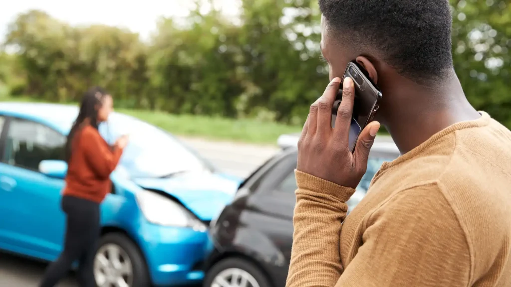 Person on the phone standing near two cars involved in a collision.