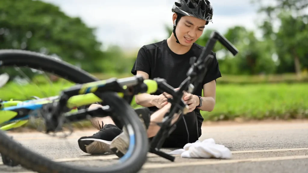 Bicyclist inspecting bike after falling, wearing helmet.